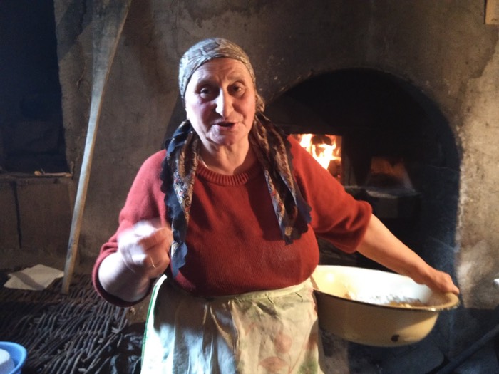 A woman cheesemaker in front of a fire with a bowl of curds on her hip