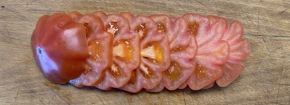 Slices of a ribbed tomato on a wooden cutting board