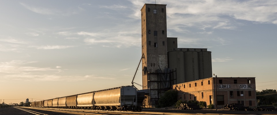 A grainelevator in Texas with freight train alongside illuminated by a low sun