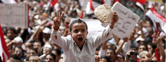 A boy holds up a loaf of bread while making a peace symbol at Tahrir Square in 2011