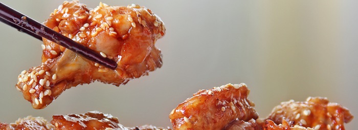 Sesame coated chicken wing held in chopsticks above a plate of similar wings