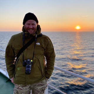 Harry Robson on board a boat with the sun near the horizon