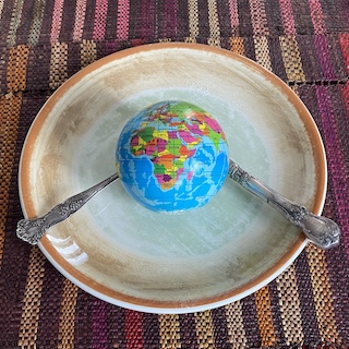 A today world globe on a plate with a knife and fork, all on a multicoloured striped table mat.