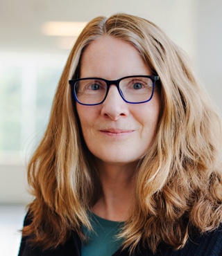 Portrait of a woman with shoulder-length light brown hair wearing blue-framed spectacles